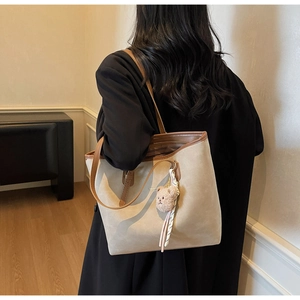 Detail view of beige suede tote bag with brown leather straps and plush bear charm
