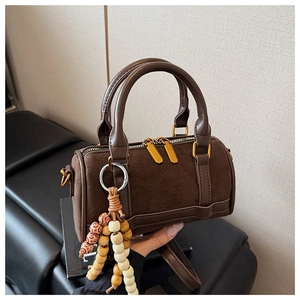 Close-up of brown suede Boston bag featuring double zippers and a vintage beaded pendant
