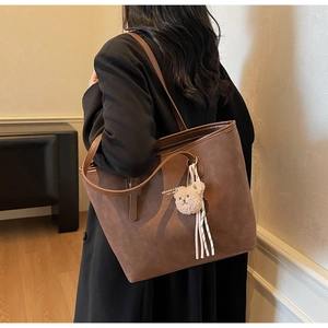 Dark brown tote bag detail with plush bear charm and ribbon on model's shoulder