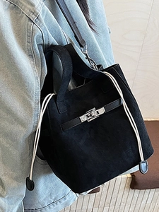 Minimalist black suede bucket bag with silver clasp shown on shoulder over denim