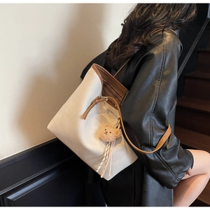 Detailed view of cream tote bag with brown leather trim and cute bear charm on a model
