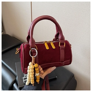 Detail of burgundy cylinder bag with suede texture and decorative wooden beads