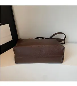 Detailed side view of dark brown litchi grain leather tote bag showing stitching and base