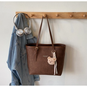 Detail of dark brown tote bag with plush bear charm and striped ribbon on a hook