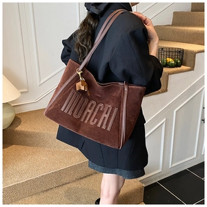 Detail of dark brown suede tote bag with MUACAI letter patch and leather straps