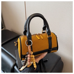 Detail view of mini Boston bag in yellow suede with leather trim and ethnic wood bead charm