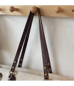 Détail du sac fourre-tout en PU crème avec bandoulière marron et rivets dorés