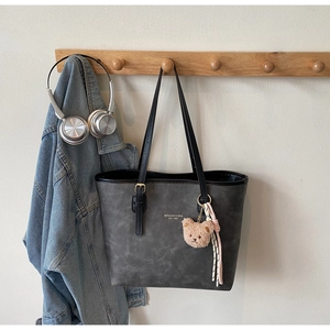 Detail of dark grey tote bag with bear charm and text hanging on a wooden hook