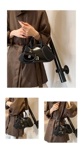 Detail view of black patent leather shoulder bag with white contrast stitching and mini pouch