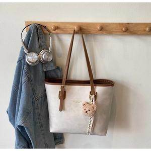 Close-up of beige tote bag with brown leather straps and cute plush bear accessory
