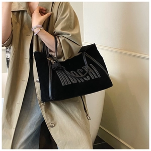 Detail of black tote bag with white stitching text worn with a khaki trench coat