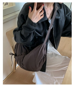 Détail du sac croissant à carreaux sombres avec nœud décoratif et bandoulière quadrillée