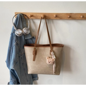 Detail of khaki leather tote bag with dark brown trim and pink plush bear charm
