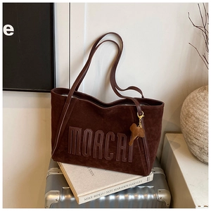Detail of dark brown suede tote bag with embossed logo and elephant charm on a suitcase