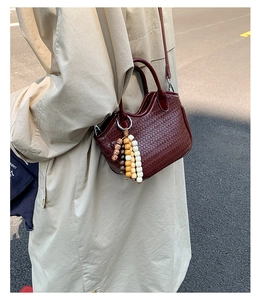 Détail d'un sac à main tissé rouge foncé avec breloque perlée et bandoulière en cuir chic