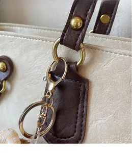 Détails des crochets dorés et attaches en cuir marron sur le sac cabas blanc crème