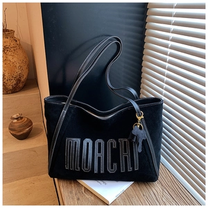 Detail of black suede tote bag with MOACAI letter patch and white contrast stitching