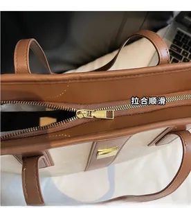 Gros plan détaillé sur la fermeture éclair dorée du sac cabas marron et beige