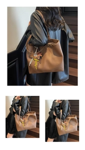 Detail of a brown leather tote bag with a cute bear pendant and litchi texture finish