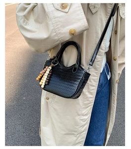 Détail d'un sac seau tressé noir avec pompon en perles de bois colorées sur un mannequin
