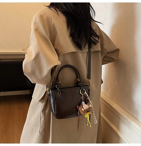 Borsa in pelle cerata marrone scuro su modella con tracolla e ciondolo a orsetto