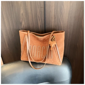 Close-up of brown suede tote bag with embossed MOACHI lettering and elephant charm on a chair