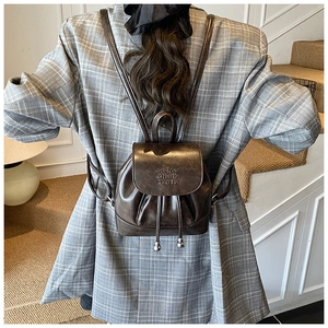 Detail showing back view of brown leather mini backpack on a grey checkered suit