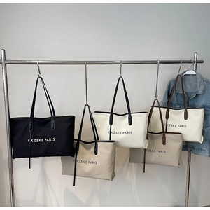 Détail de sacs cabas en toile noir, crème et beige suspendus sur un cintre en métal