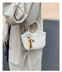 Détail du sac seau tressé blanc cassé avec gland en perles et bordure ondulée