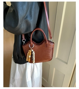 Détail d'un sac seau tressé avec pompon en perles de bois et bandoulière amovible