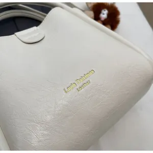 Close-up of white lychee pattern faux leather handbag with gold embossed logo detail