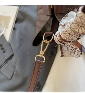 Détail du sac à main tissé marron foncé montrant les crochets dorés et le foulard en soie