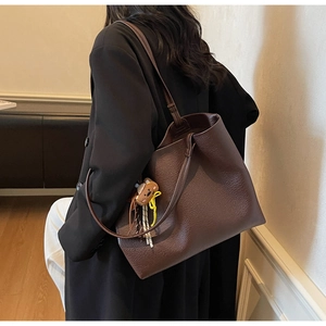 Detail view of large brown pebble leather tote bag with a cute bear plush pendant on shoulder