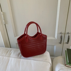 Détail d'un sac à main en cuir tressé rouge avec texture sur fond de canapé blanc