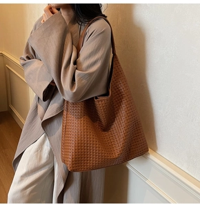 Détail de la texture d'un sac cabas tissé caramel porté à l'épaule par un mannequin
