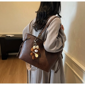 Détail d'un sac cabas en similicuir marron café avec charme ours porté à l'épaule
