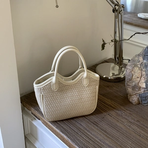 Vue détaillée du sac à main tissé crème sur un bureau en bois au décor minimaliste