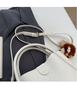 Detail of white litchi pattern bag with golden buckle and brown plush pendant