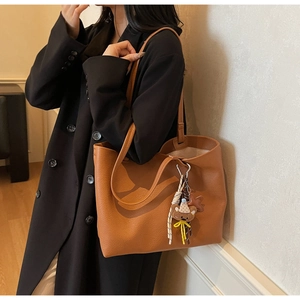 Brown large capacity tote bag with litchi texture and cute bear charm shown on shoulder