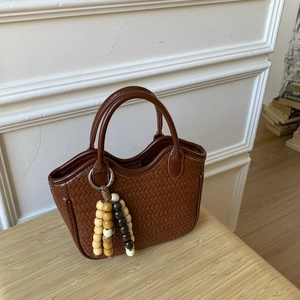 Détail d'un sac à main tissé marron avec pompon en perles de bois sur table en bois