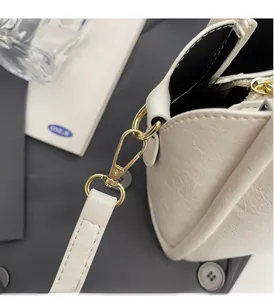 Close-up of off-white lychee texture handbag with golden metal carabiner and black lining