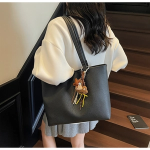 Detail of black pebbled leather tote bag with brown plush bear charm and twin shoulder straps