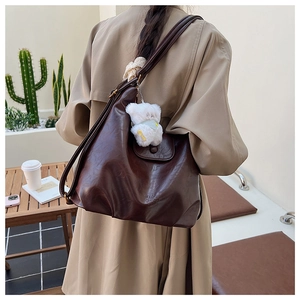 Vue latérale d'un grand cabas en cuir PU marron foncé avec pendentif ours blanc sur modèle