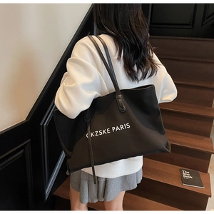 Vue détaillée d'un grand sac cabas en toile noire avec lettrage blanc porté par un mannequin