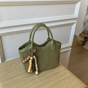 Détail du sac à main vert tressé avec poignée en cuir et pendentif en perles de bois