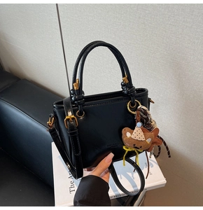 Dettaglio ravvicinato di una borsa a tracolla in pelle cerata nera con ciondoli decorativi