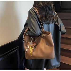 Detailed texture of brown pebble leather tote bag with bear charm on model's shoulder