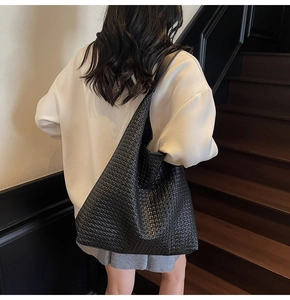 Détail d'un grand sac hobo tressé noir porté par un mannequin dans un décor minimaliste