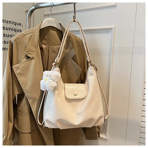 Détail d'un sac hobo en cuir beige avec fermeture à pression et breloque petit ours