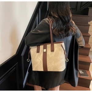 Détail d'un sac cabas beige texturé avec des lanières marron foncé et des pièces dorées